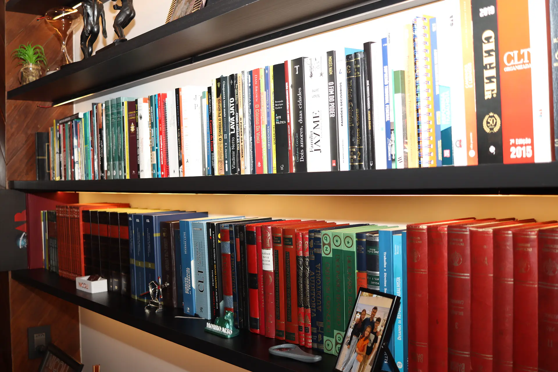 Estante iluminada com livros jurídicos, obras de direito do trabalho e coleções encadernadas em vermelho