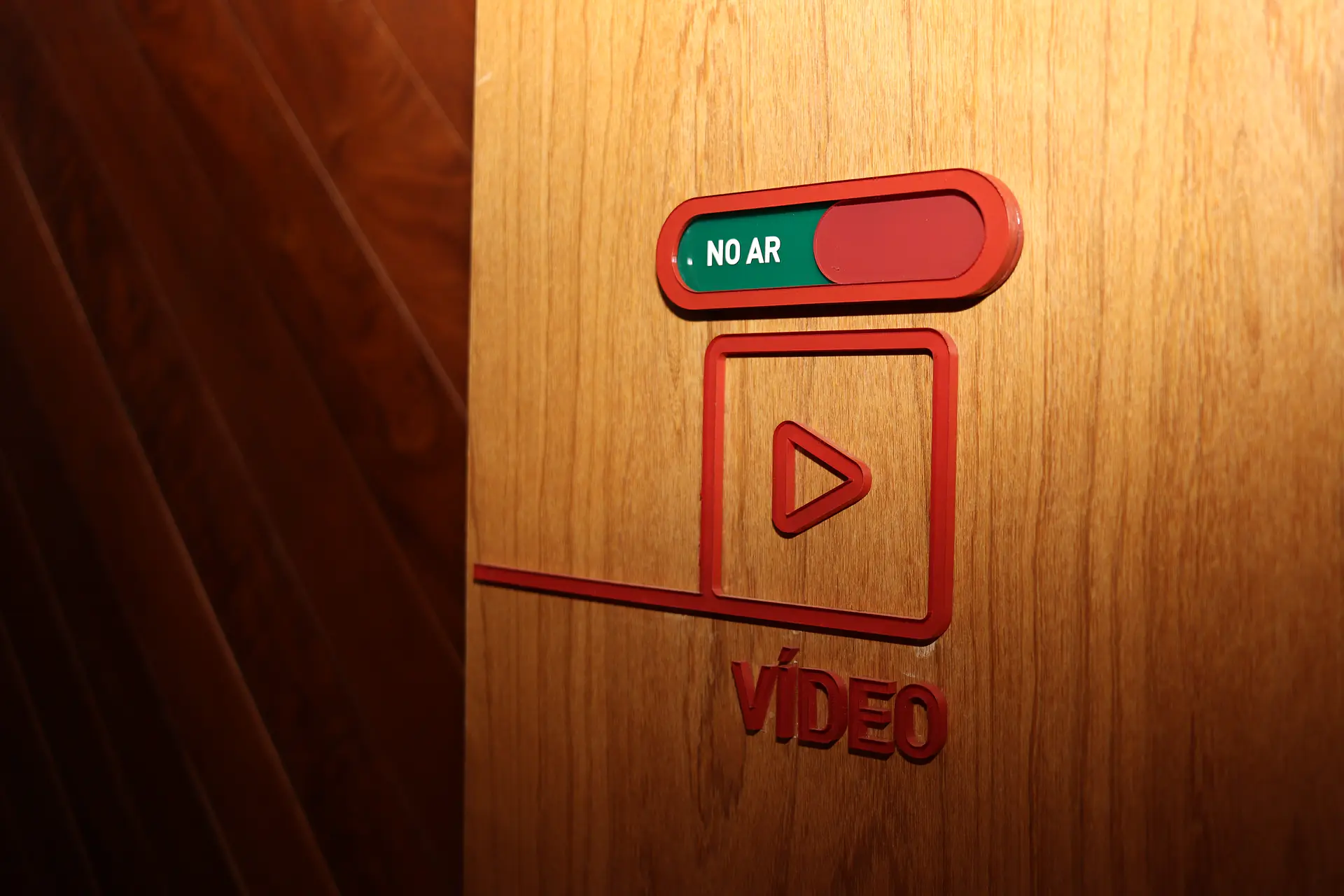 Sinalização "No ar" e "Vídeo" em acrílico vermelho e verde sobre a porta de madeira do estúdio de gravação do escritório